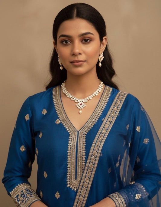 Woman wearing a blue embroidered traditional outfit with jewelry against a beige background