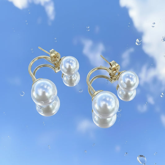 Pair of pearl earrings on a reflective blue surface with sky reflection
