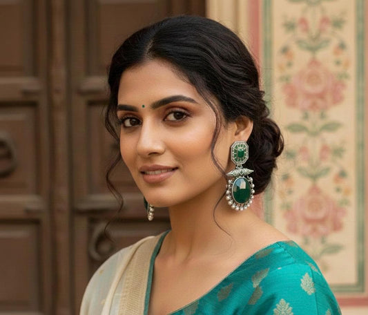 Woman wearing a teal saree with green and silver earrings in an indoor setting.