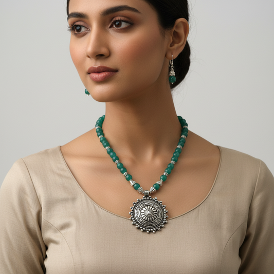 Woman wearing a green beaded necklace with a large silver pendant on a plain background
