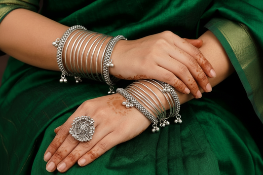 Silver jewelry including bangles and rings on a person's hands with a green fabric background.