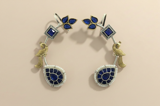 Pair of cuff earrings with blue stones and gold accents on a beige background