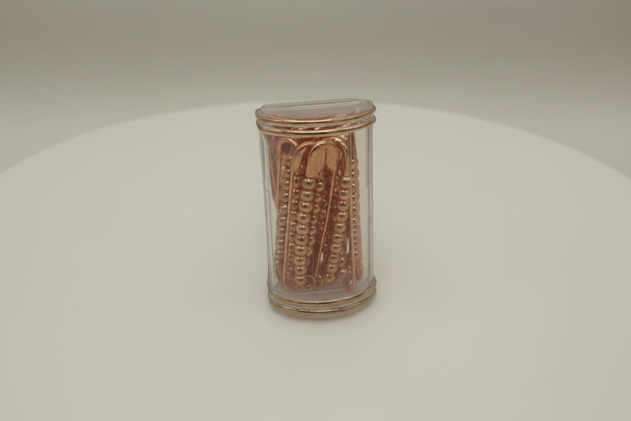 Small cylindrical metallic safty pins with embossed design on a white background