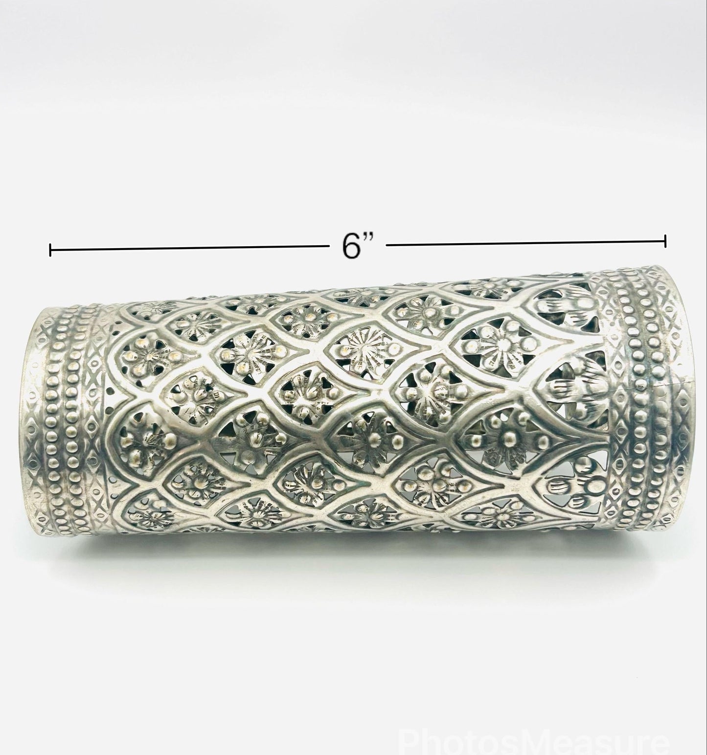 Decorative silver cylindrical object with intricate patterns on a white background