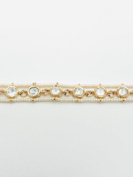 Two gold bracelets with pearl and crystal accents on a light gray background
