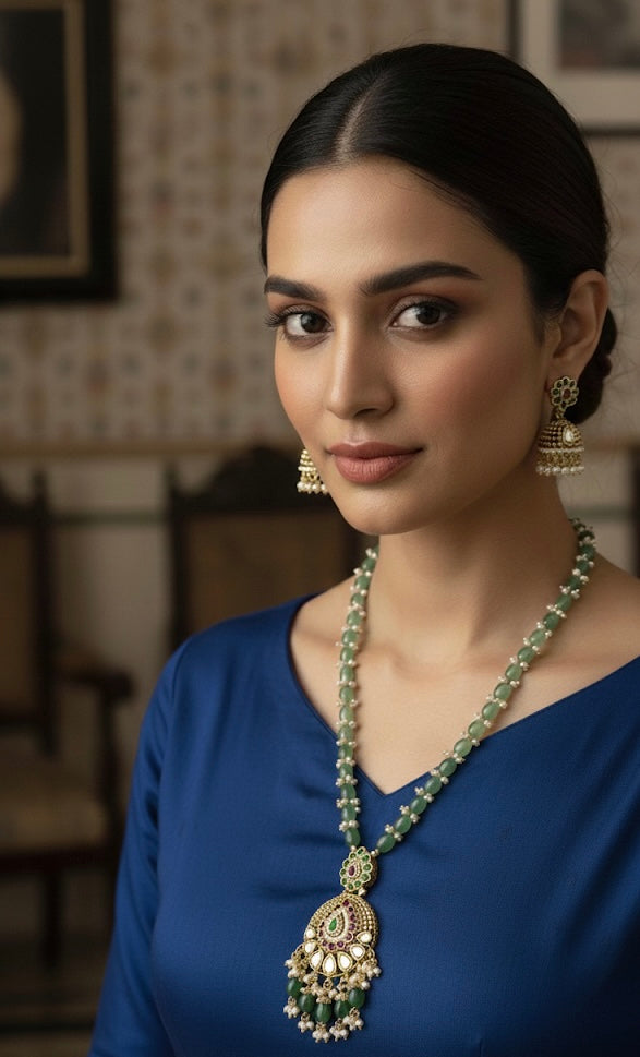 Woman wearing a blue top and green necklace with earrings indoors