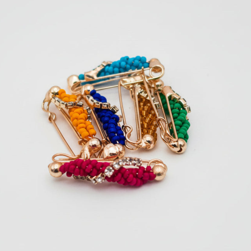 Decorative safty pins with multicolored gemstones on a light gray background