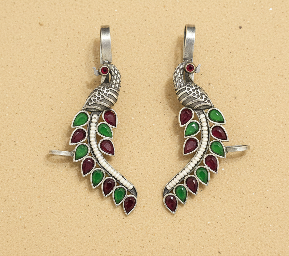 Two silver peacock-shaped pendants with green and red accents on a beige background.