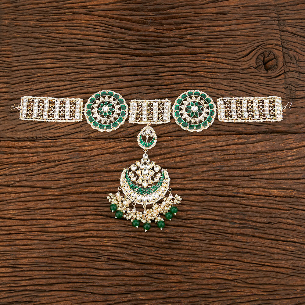 Decorative hair headband tikka with emerald green stones on a wooden surface