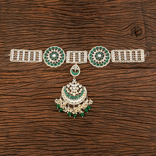 Decorative hair headband tikka with emerald green stones on a wooden surface