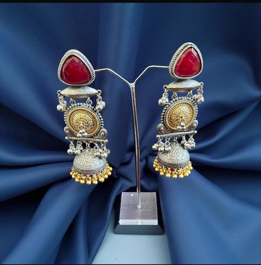 Ornate earrings with red stones on a blue fabric background