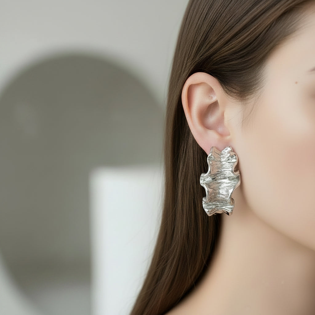 Silver leaf-shaped earring worn by a person with a neutral background