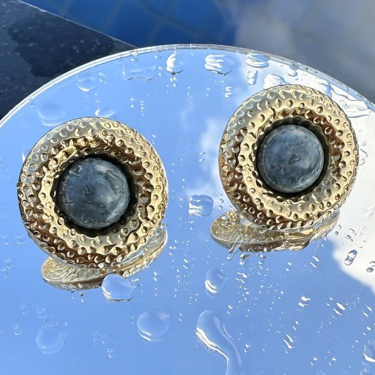 Pair of gold and gray earrings on a reflective surface