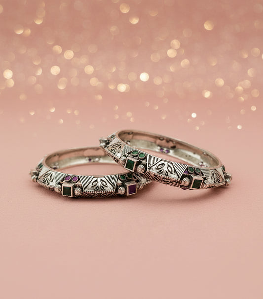 Two silver bangles with gemstone accents on a light gray background
