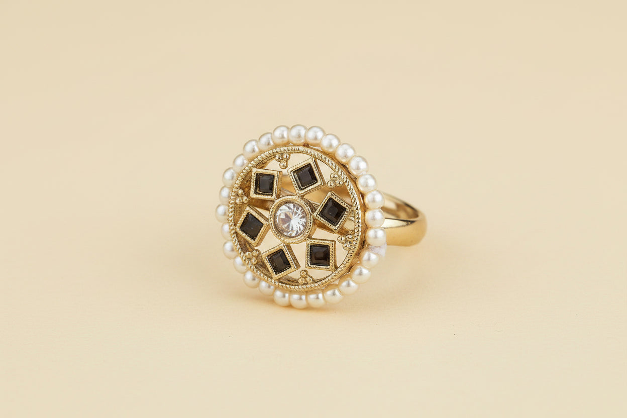 Gold plated black kundan statement ring with pearl and gemstone design on a light being background 