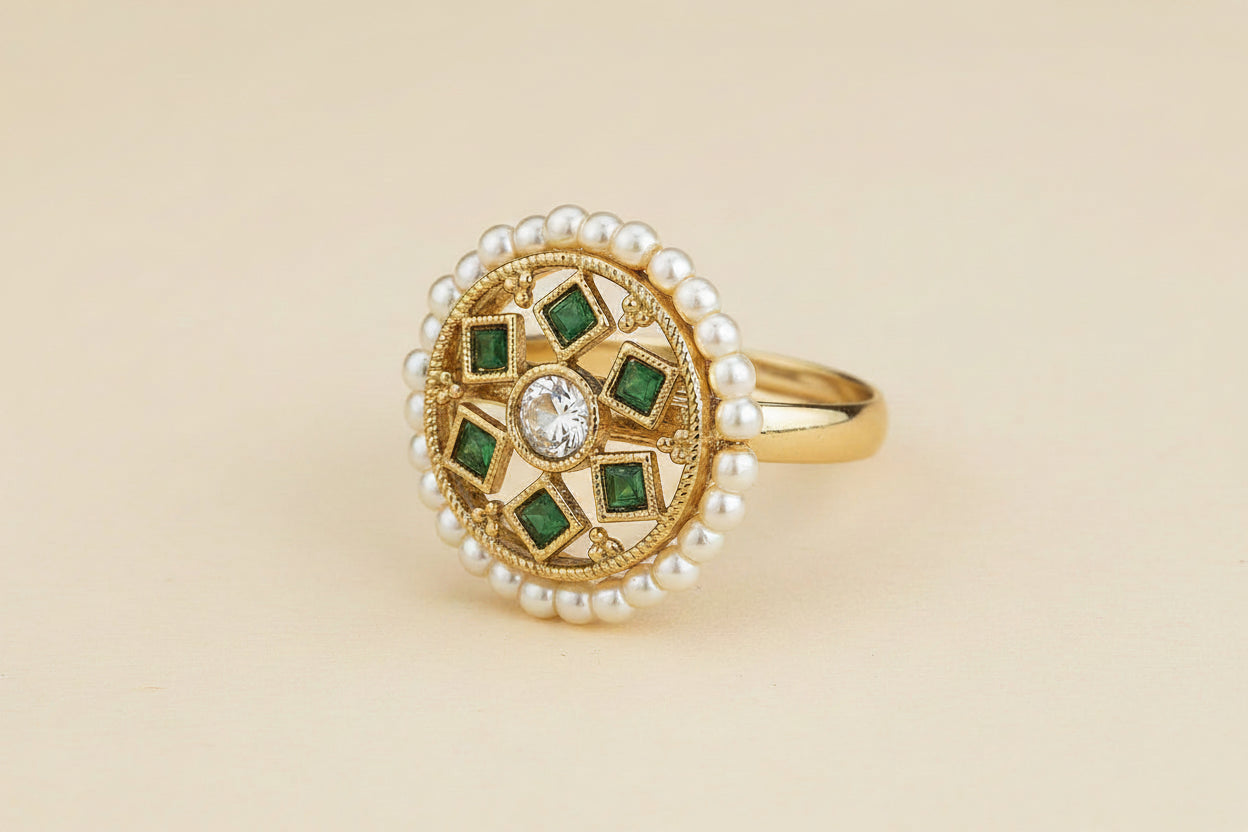 antique Gold  plated ring with green gemstones and pearl accents on a light being background 