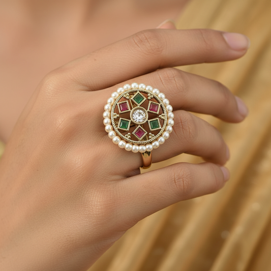 Close-up of a hand wearing a decorative red green stone antique ring with pearls and gemstones against a blurred background