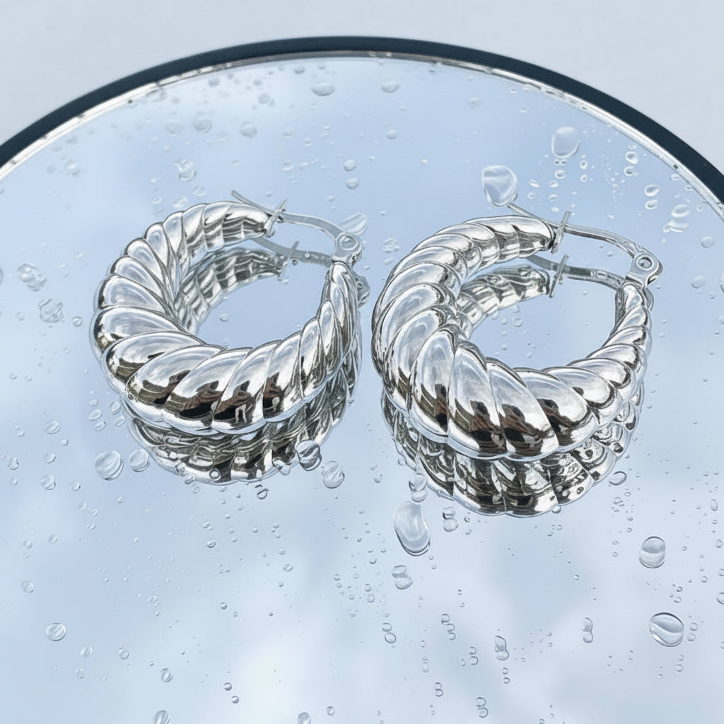 Silver hoop earrings on a glass surface with water droplets.
