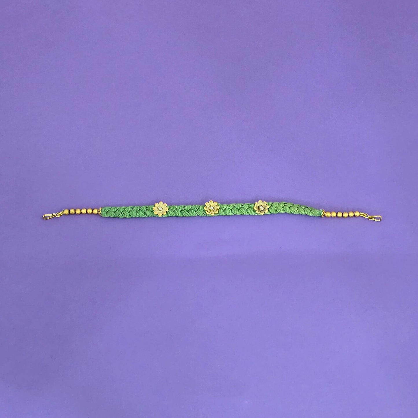 Green braided head band with gold beads and flowers on a purple background