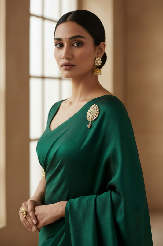 Woman wearing sari dupatta kudan brooch a green saree with gold jewelry against a neutral background