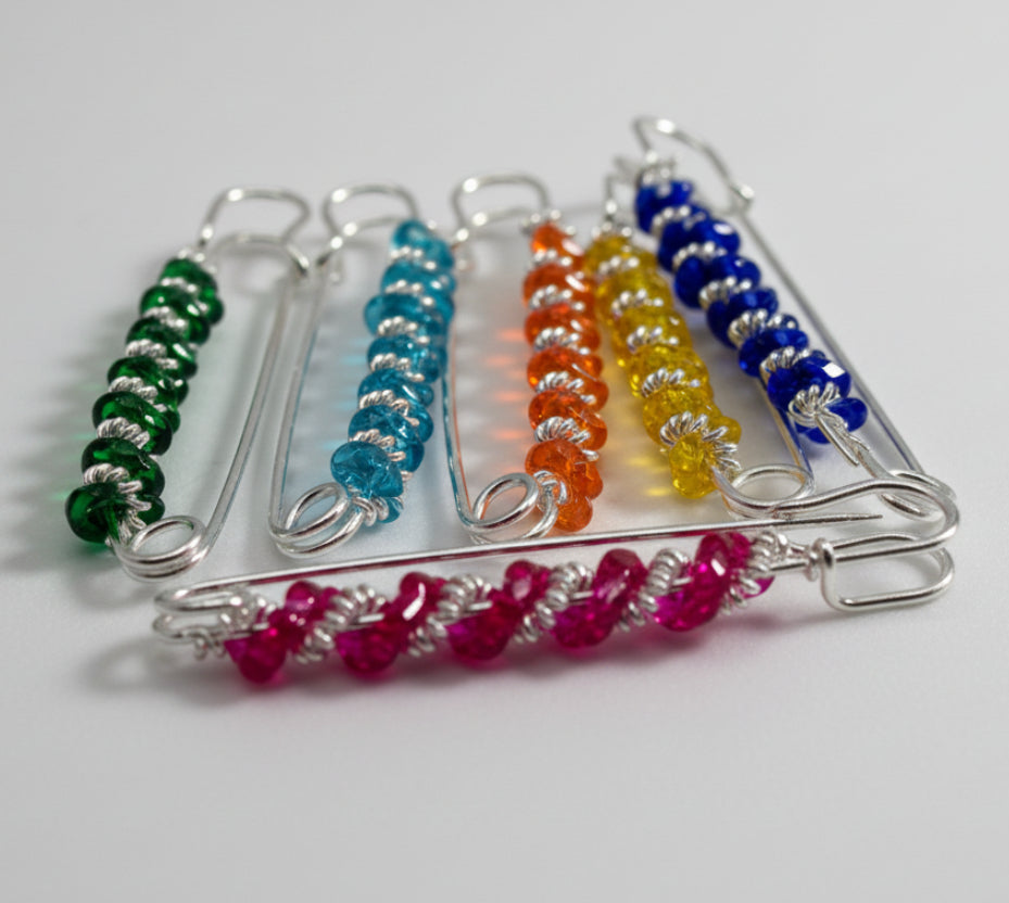 decoretive safty pins in multi colors on a white background