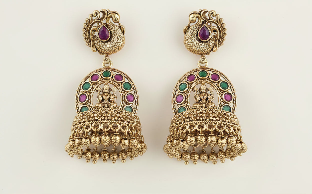 temple gold plated earrings with ruby red and green gemstones on a being background