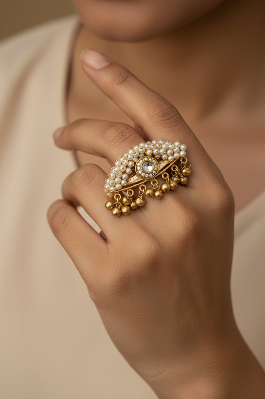 Gold ring with pearls and gemstones on a hand against a neutral background