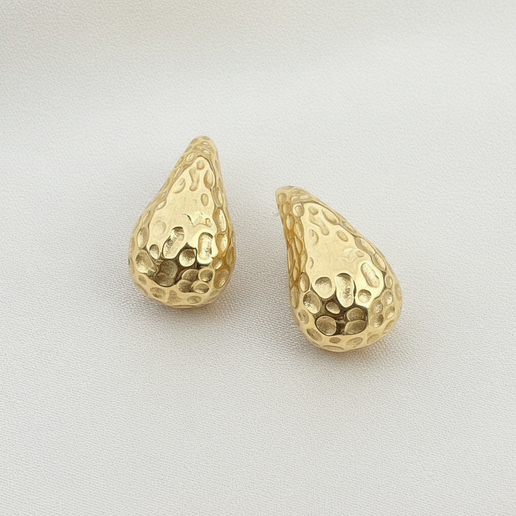 Gold textured earrings on a round metallic surface with a blue tiled background