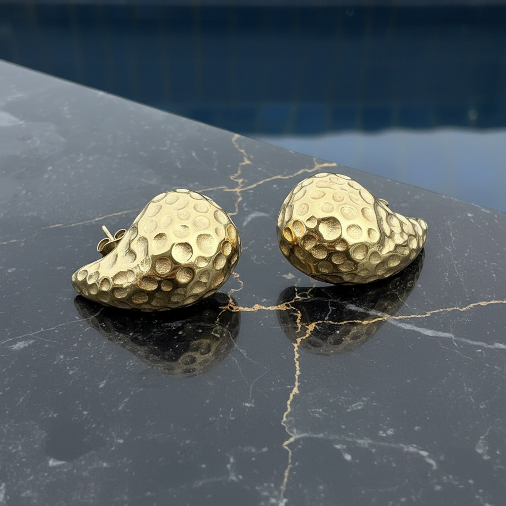 Gold textured earrings on a dark marble surface
