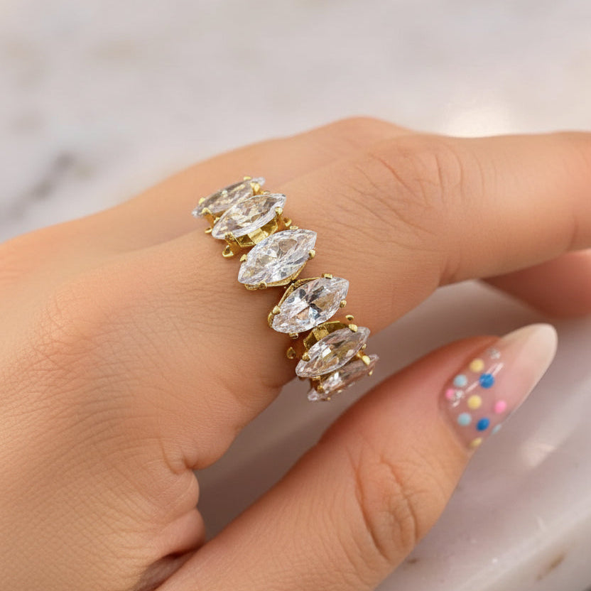 Gold ring with clear gemstones on a finger against a marble background