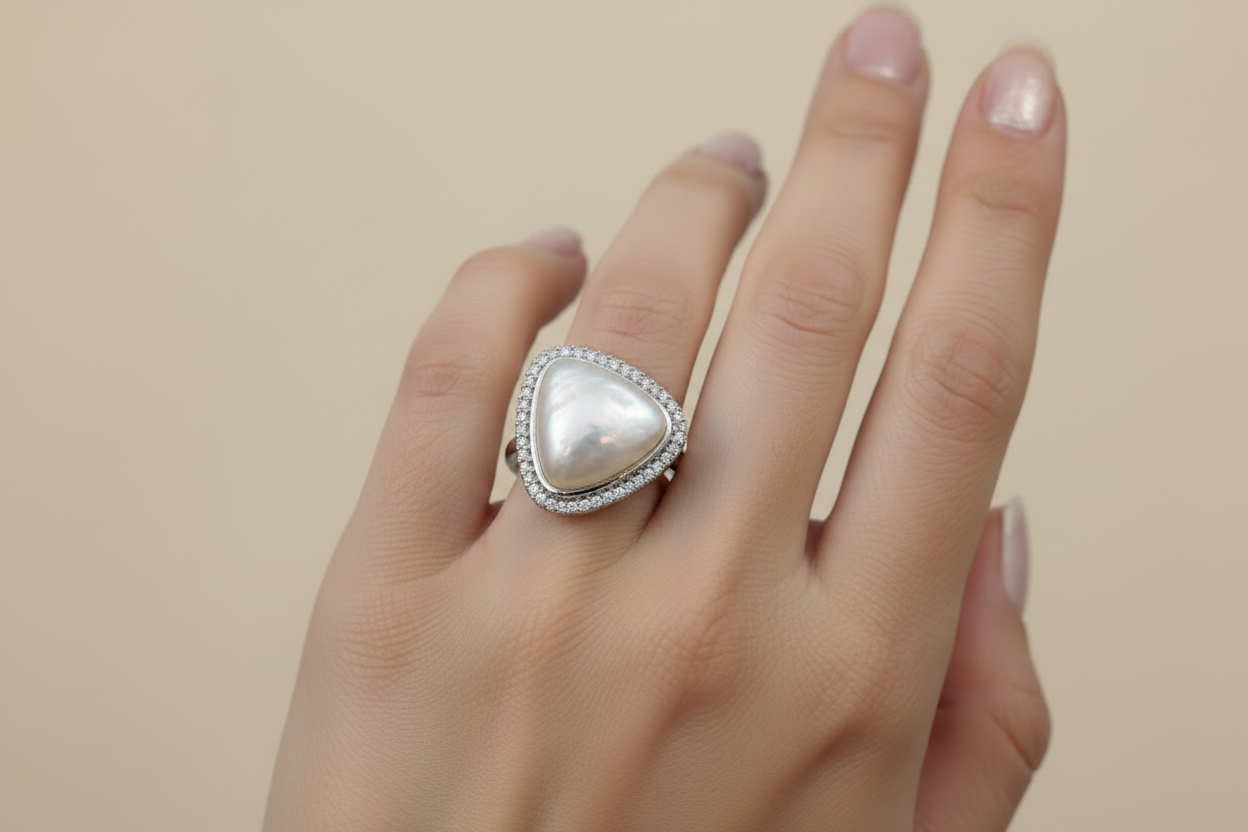 Hand wearing a ring with a large pearl-like stone on a neutral background