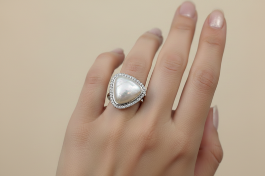 Hand wearing a ring with a large pearl-like stone on a neutral background