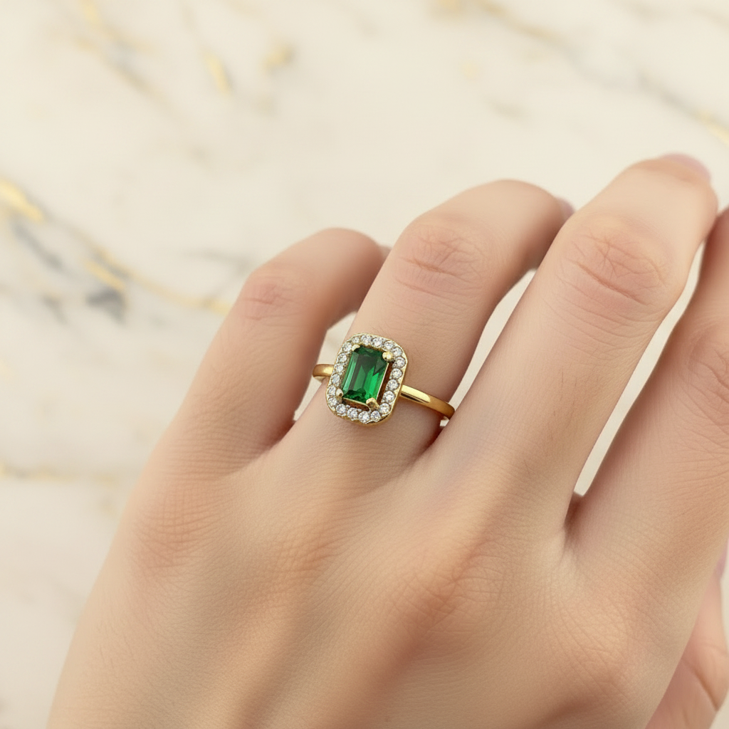 Gold ring with a green gemstone on a hand against a light background