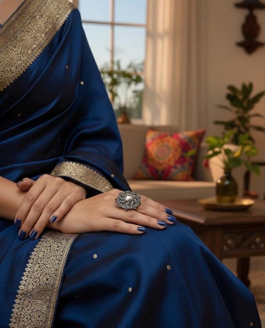 Person wearing a blue saree with gold border in a living room setting