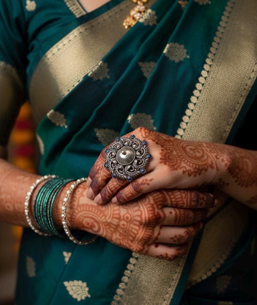 Person wearing a teal saree with gold border, holding hands with intricate henna designs.