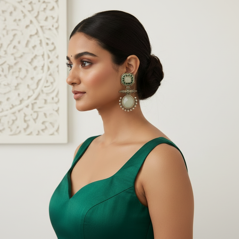 Woman wearing green earrings and a green dress against a white wall.