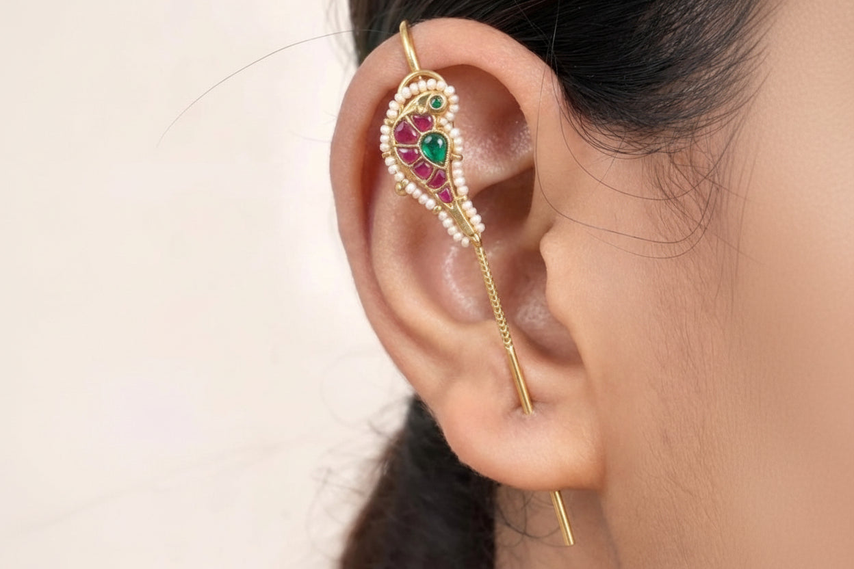 Gold ear cuff with green and red gemstones worn by a person