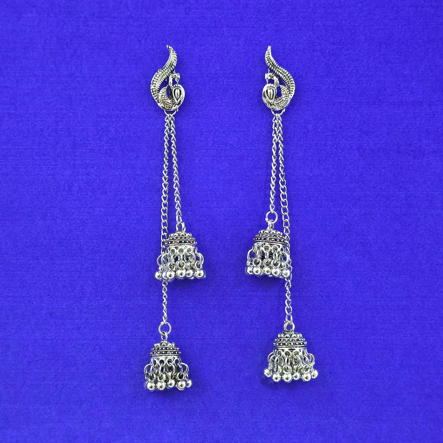 Pair of silver earrings with jhumka designs on a blue background