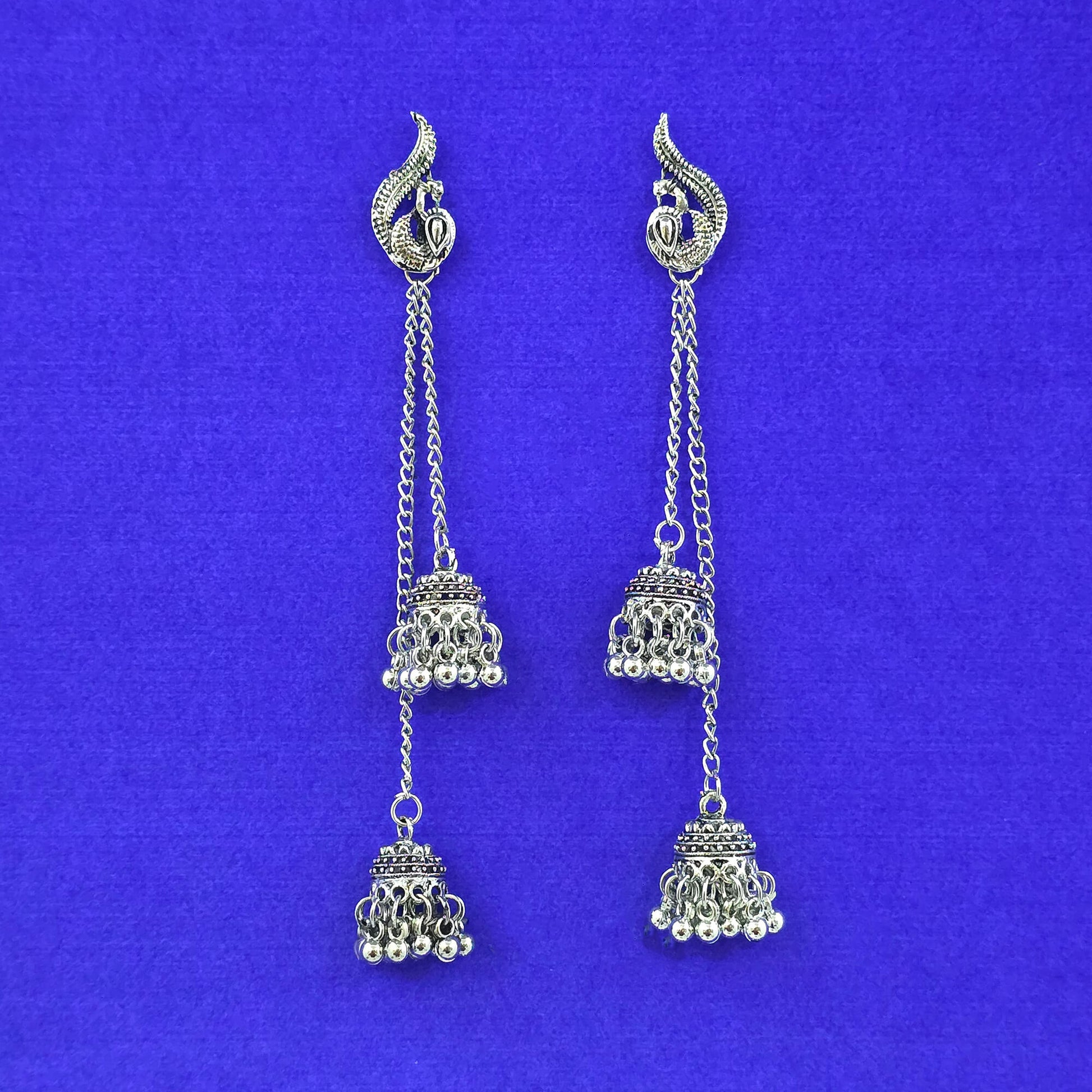 Pair of silver earrings with jhumka designs on a blue background