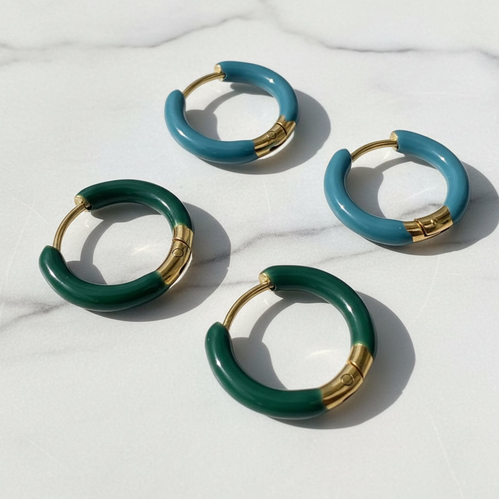 Four green hoop earrings with gold accents on a textured surface.