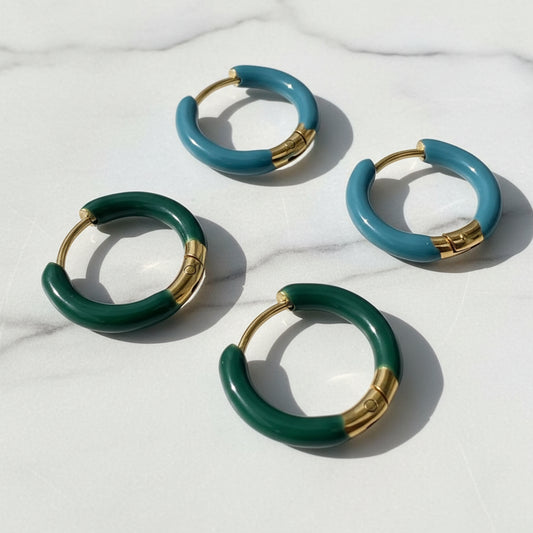 Four green hoop earrings with gold accents on a textured surface.