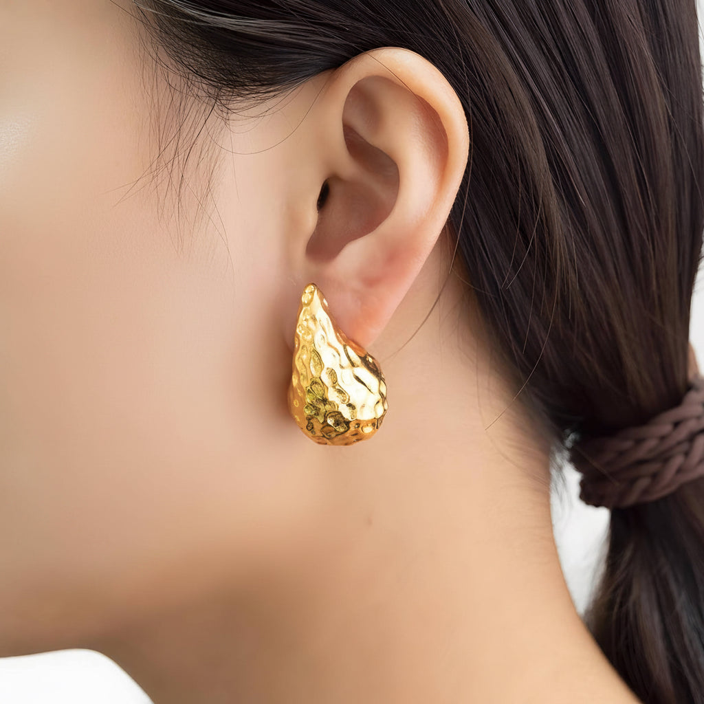 Gold earring worn by a person with dark hair tied back.