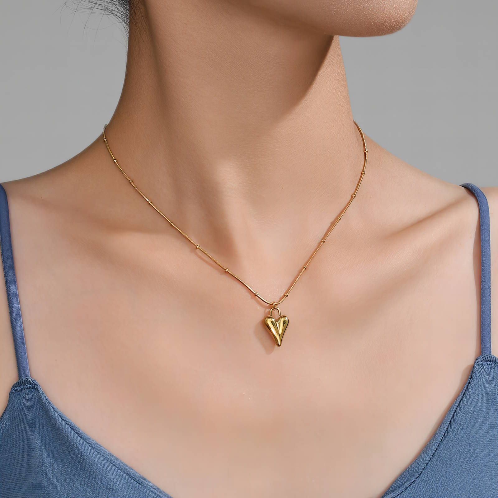 Gold necklace with a triangle pendant worn by a person in a blue top against a gray background