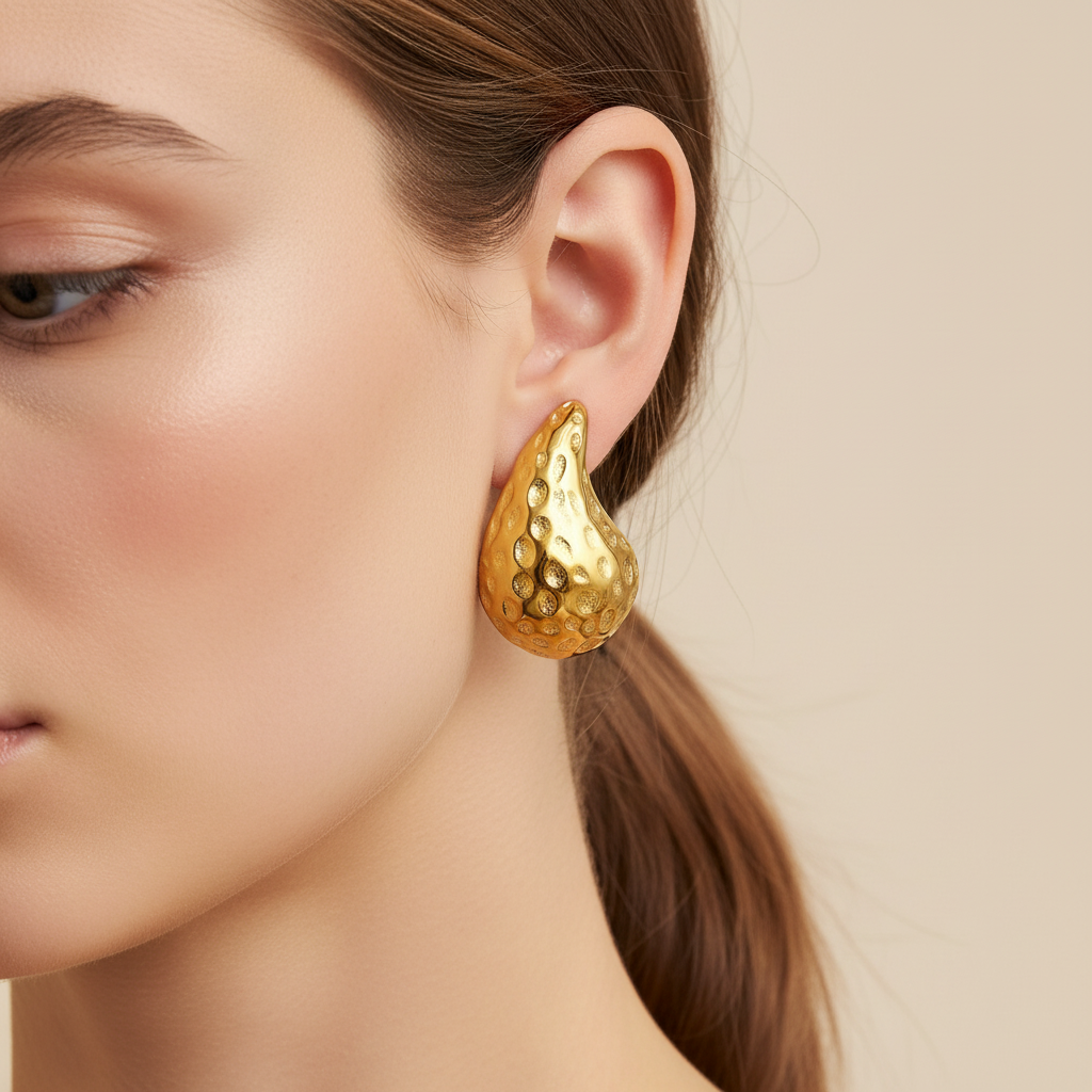 Gold earring worn by a model on a beige background