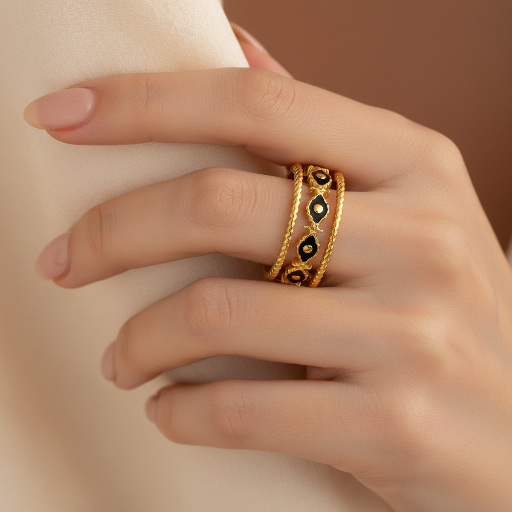 Gold ring with black accents on a hand against a neutral background
