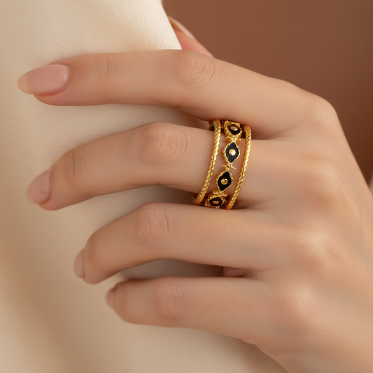 Gold ring with black accents on a hand against a neutral background