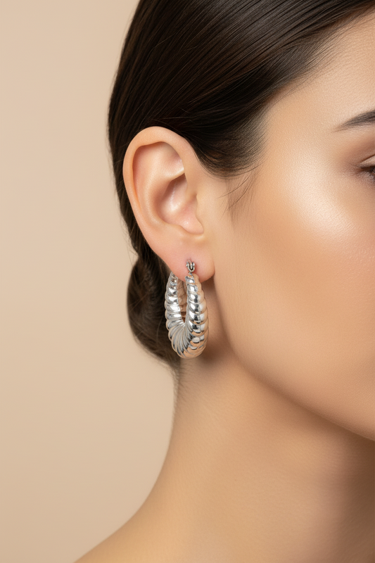 Close-up of a woman wearing silver hoop earrings against a beige background