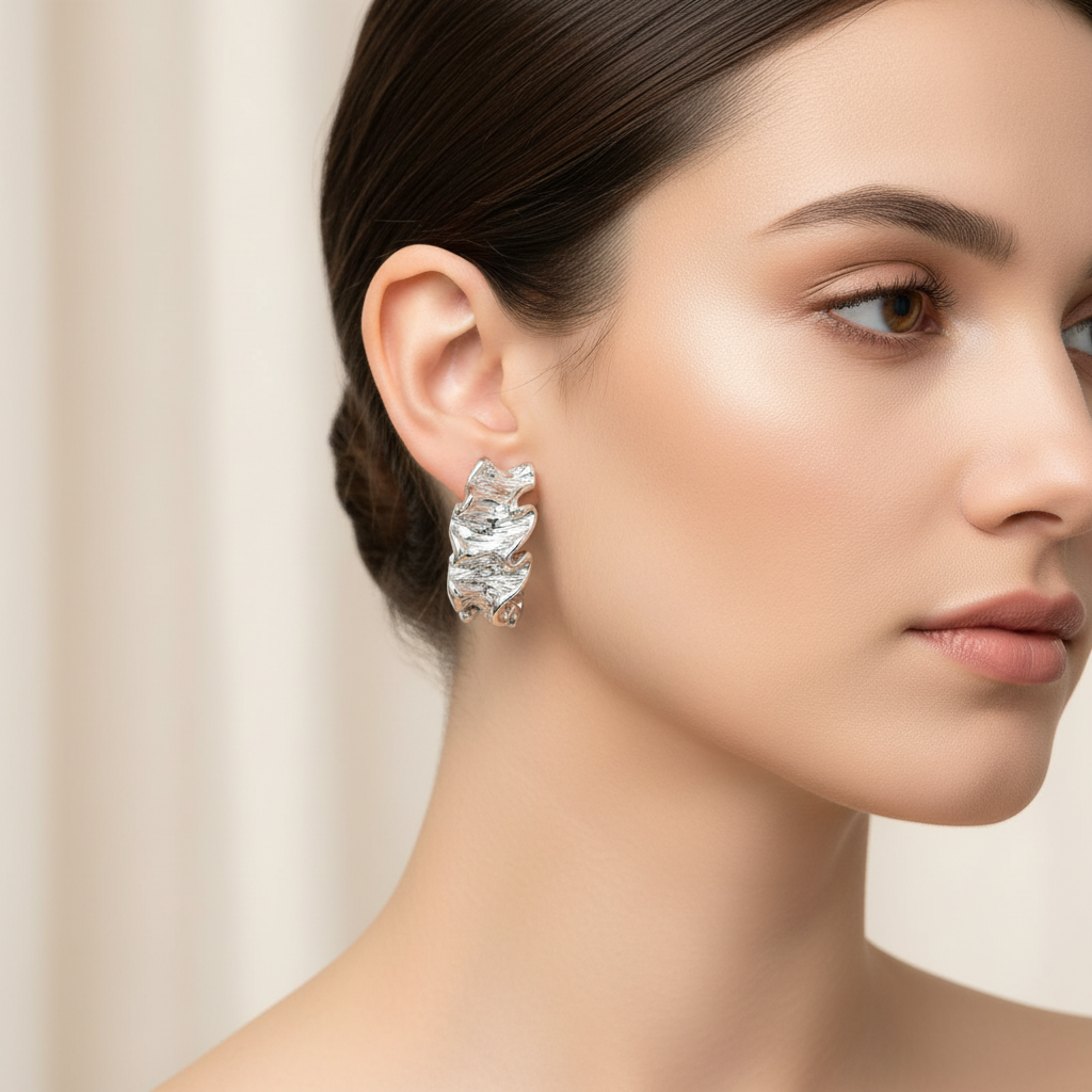 Close-up of a woman wearing a pair of silver earrings with a beige background