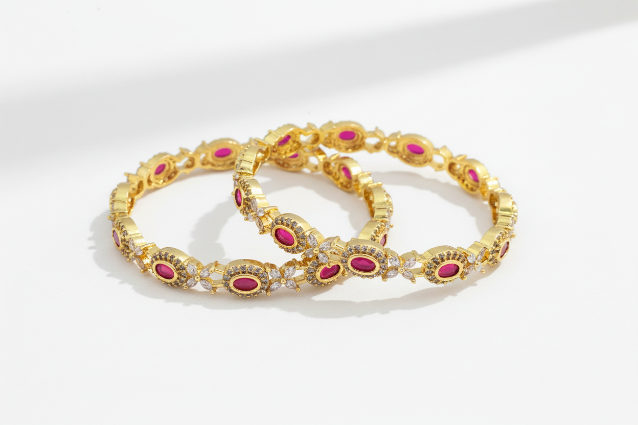 Pair of gold bangles with pink stones on a white background