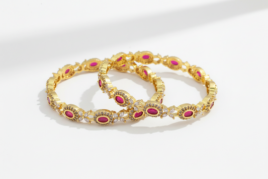 Pair of gold bangles with pink stones on a white background